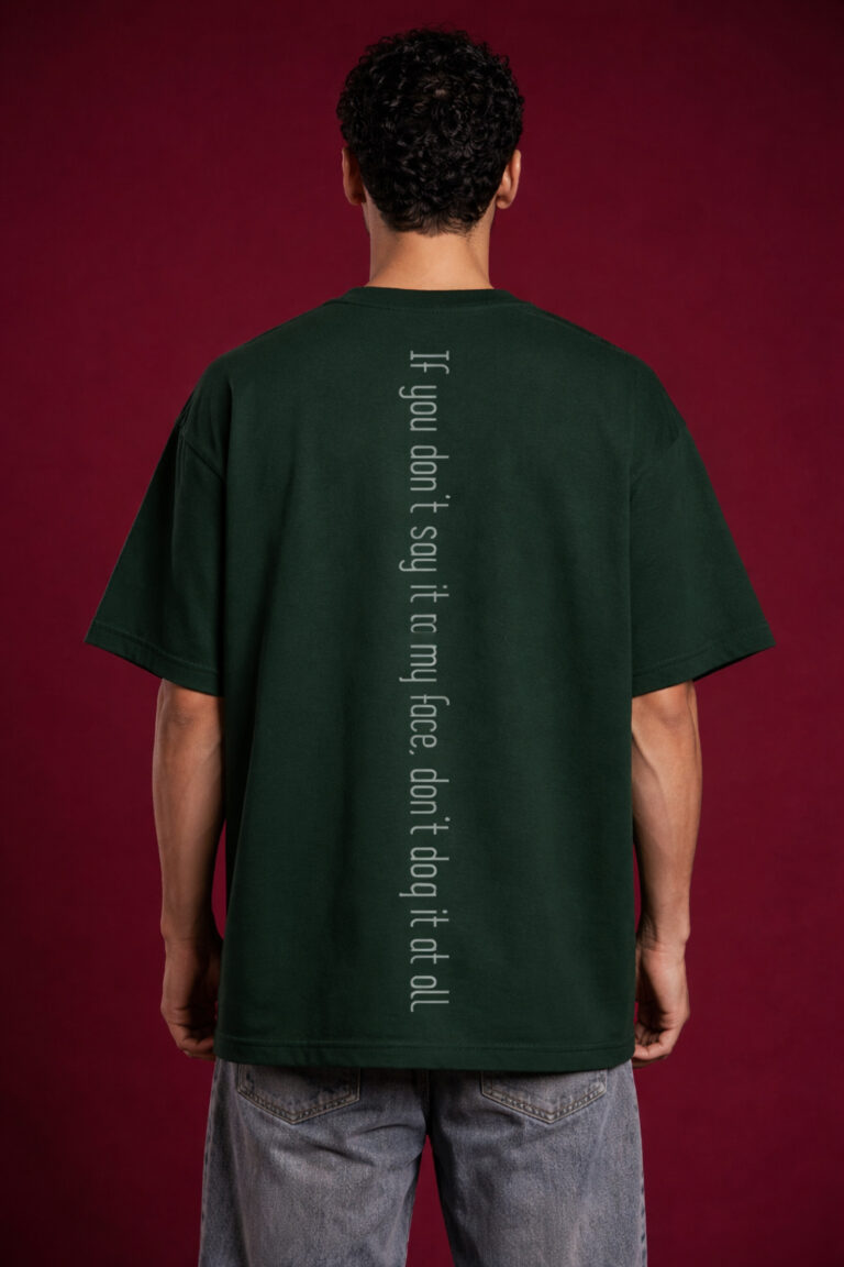 Back view of a boxy fit dark green streetwear t-shirt showing a vertical spine-aligned text graphic that reads 'If you don't say it to my face, don't dog it at all.' Minimalist streetwear design with drop shoulder construction on a male model.