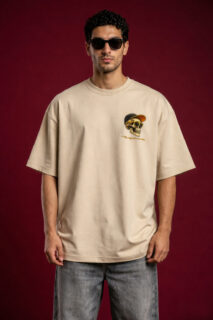 Man wearing oversized beige t-shirt with small skull graphic on chest, streetwear style, neutral background