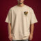 Man wearing oversized beige t-shirt with small skull graphic on chest, streetwear style, neutral background