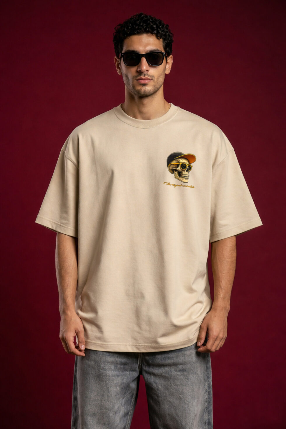 Man wearing oversized beige t-shirt with small skull graphic on chest, streetwear style, neutral background