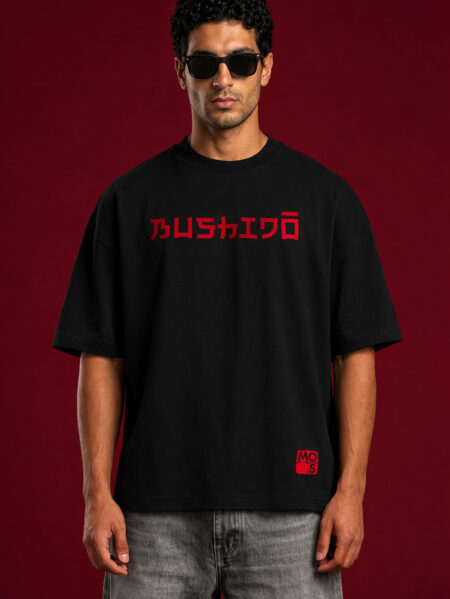 Front view of a black oversized streetwear t-shirt featuring the word "BUSHIDO" in red Japanese-inspired typography across the chest, styled with grey denim on a male model.