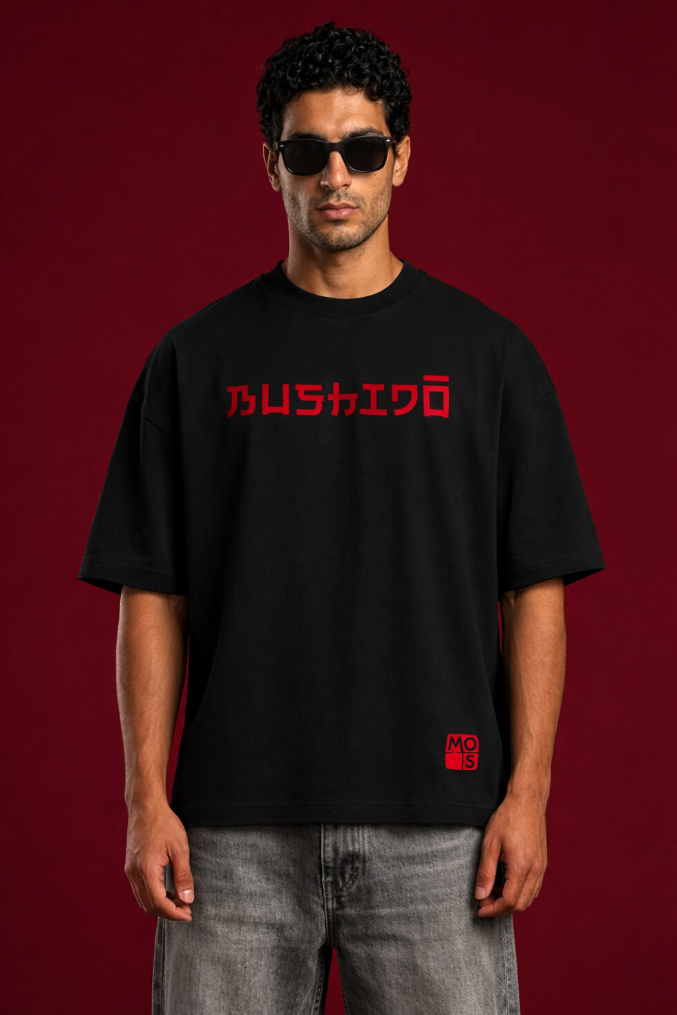 Front view of a black oversized streetwear t-shirt featuring the word "BUSHIDO" in red Japanese-inspired typography across the chest, styled with grey denim on a male model.
