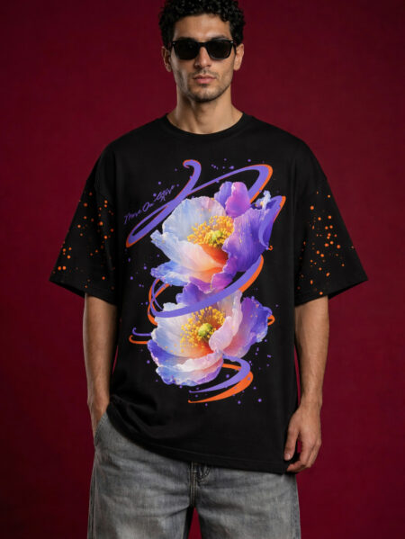 Male model wearing a black oversized streetwear t-shirt featuring a vibrant purple and blue floral graphic with orange swirl accents. The t-shirt has dropped shoulders and orange paint splatter details on the sleeves