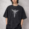 A male model wearing a premium oversized acid-wash charcoal t-shirt. The shirt features a centered white graphic of a skeletal winged angel in a 90s grunge style. The fit is boxy with drop-shoulder sleeves, styled with black trousers against a neutral industrial concrete background.