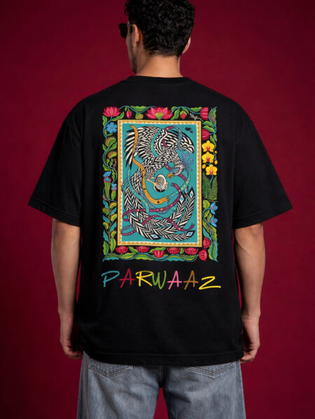 Back view of a black oversized graphic t-shirt featuring a large, vibrant South Asian truck art-inspired phoenix illustration inside a floral border, with "PARWAAZ" text printed in colorful hand-drawn font at the bottom.