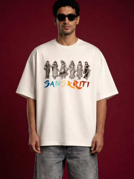 Front view of a man wearing an off-white oversized t-shirt featuring "Sanskriti" branding. The design includes a row of six traditional Indian figures in folk attire in a black linocut style, positioned above colorful brushstroke typography. The model is wearing black sunglasses and light-wash denim against a deep maroon background.