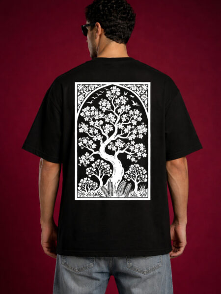 Back view of a man wearing a black oversized graphic t-shirt with a large, vertical white rectangular print of a stylized tree of life with birds and flowers. Detailed Art Nouveau inspired nature illustration on a relaxed-fit streetwear shirt