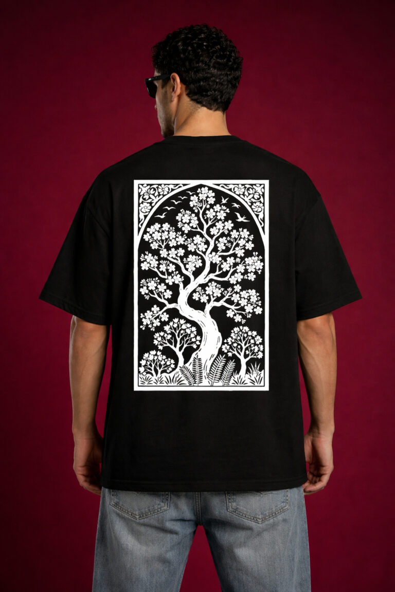 Back view of a man wearing a black oversized graphic t-shirt with a large, vertical white rectangular print of a stylized tree of life with birds and flowers. Detailed Art Nouveau inspired nature illustration on a relaxed-fit streetwear shirt