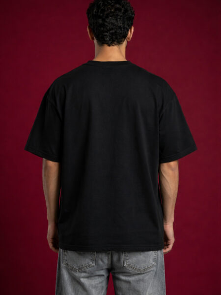 Model wearing a Wave Seekers black heavyweight boxy fit tee with a whimsical surfing animal graphic on a deep red background.