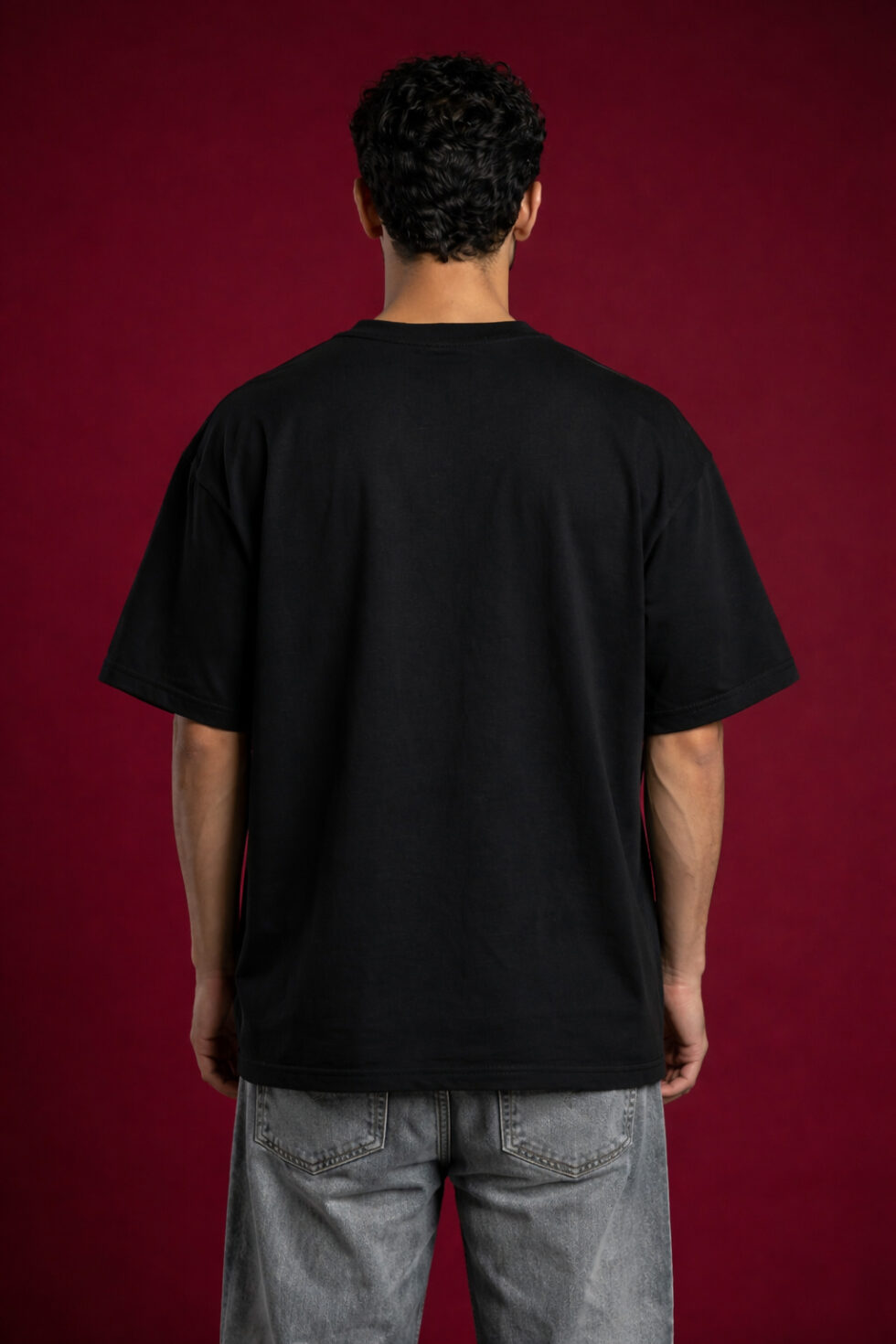 Model wearing a Wave Seekers black heavyweight boxy fit tee with a whimsical surfing animal graphic on a deep red background.