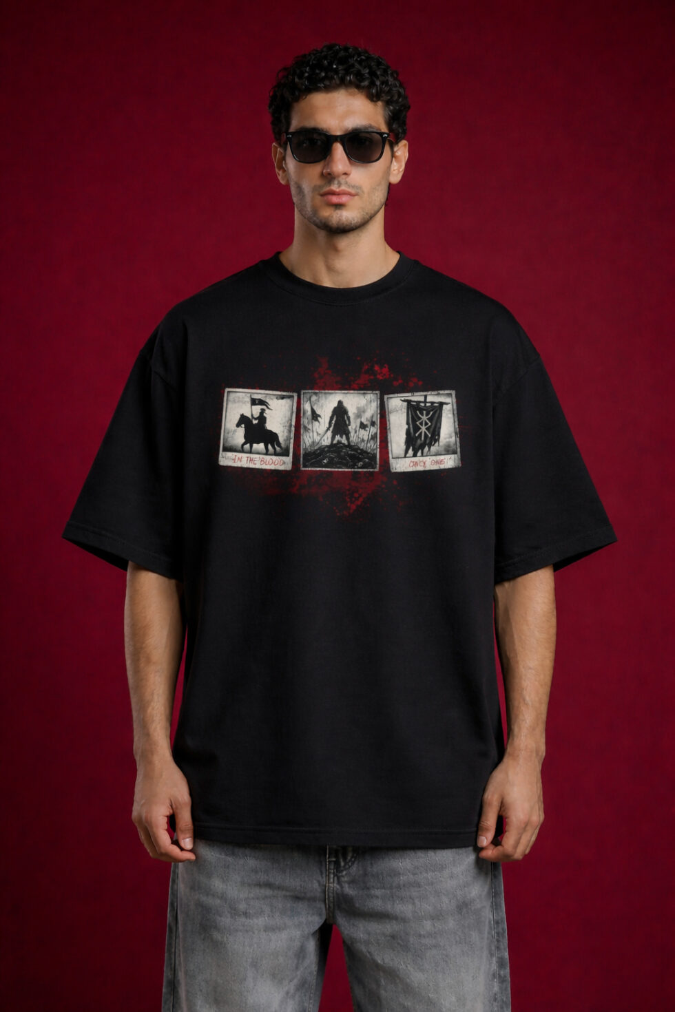 Front view of a man wearing a black heavyweight oversized t-shirt featuring three vintage polaroid-style warrior graphics on the chest with red blood-splatter accents.