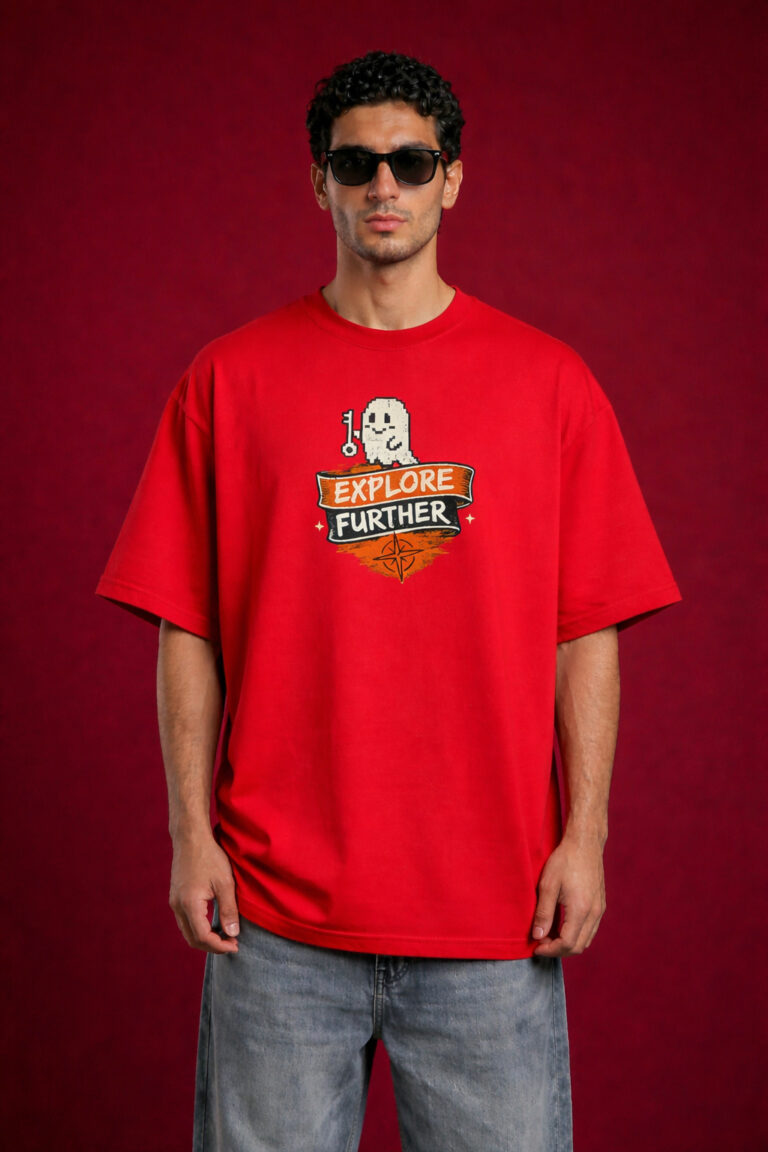 A male model wearing a bright red, oversized streetwear t-shirt. The chest features a graphic of a white pixel-art ghost holding a key above a banner that says "EXPLORE FURTHER" with a compass icon. The model is also wearing dark sunglasses and light-wash denim jeans against a deep red textured background.
