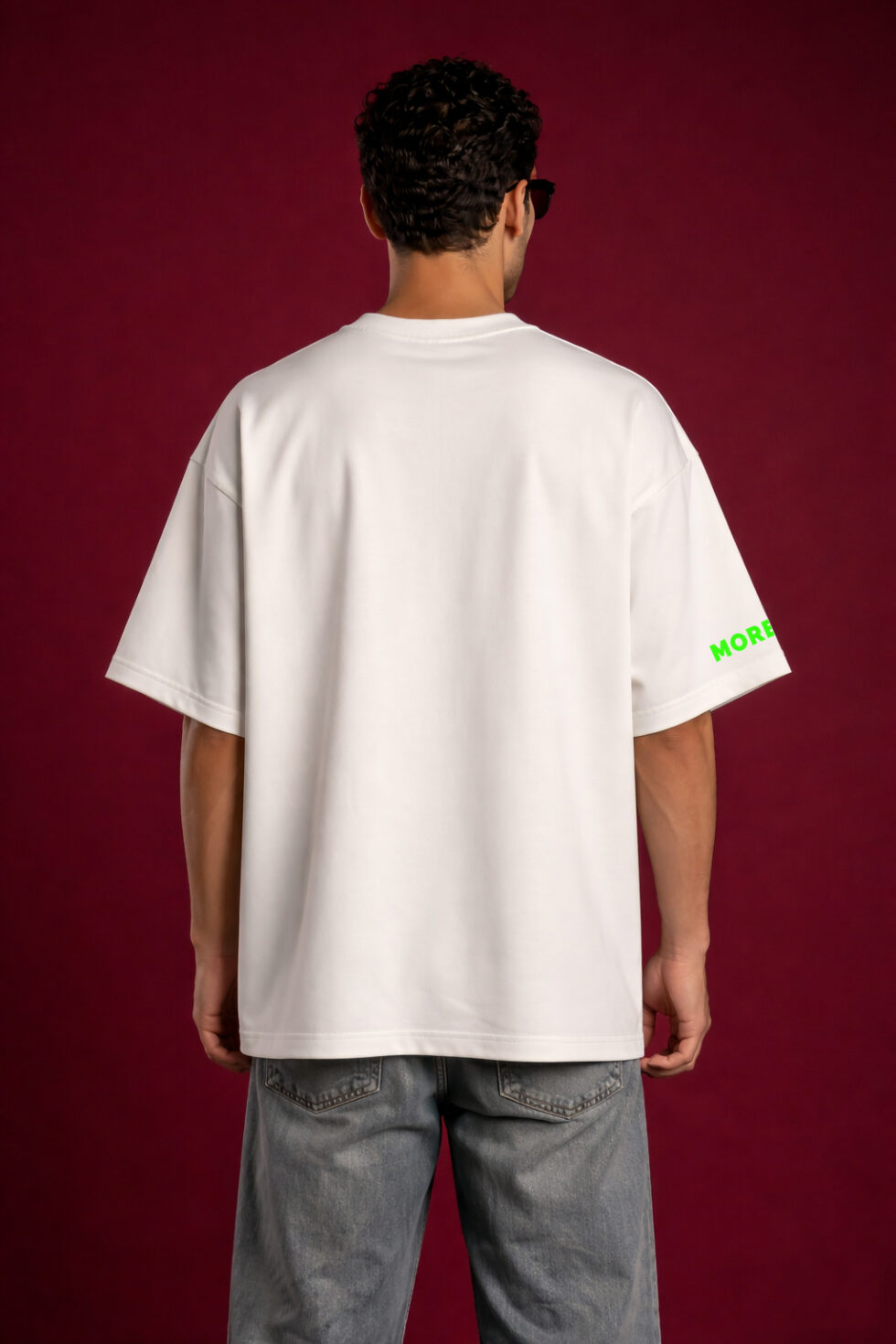 Back view of man wearing plain oversized off-white t-shirt with relaxed fit and faded grey jeans on red background