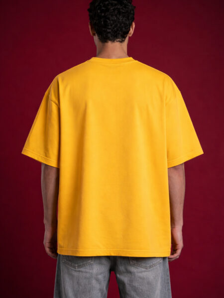 Rear view of a male model wearing a plain oversized yellow streetwear t-shirt with a drop-shoulder design and relaxed boxy fit.