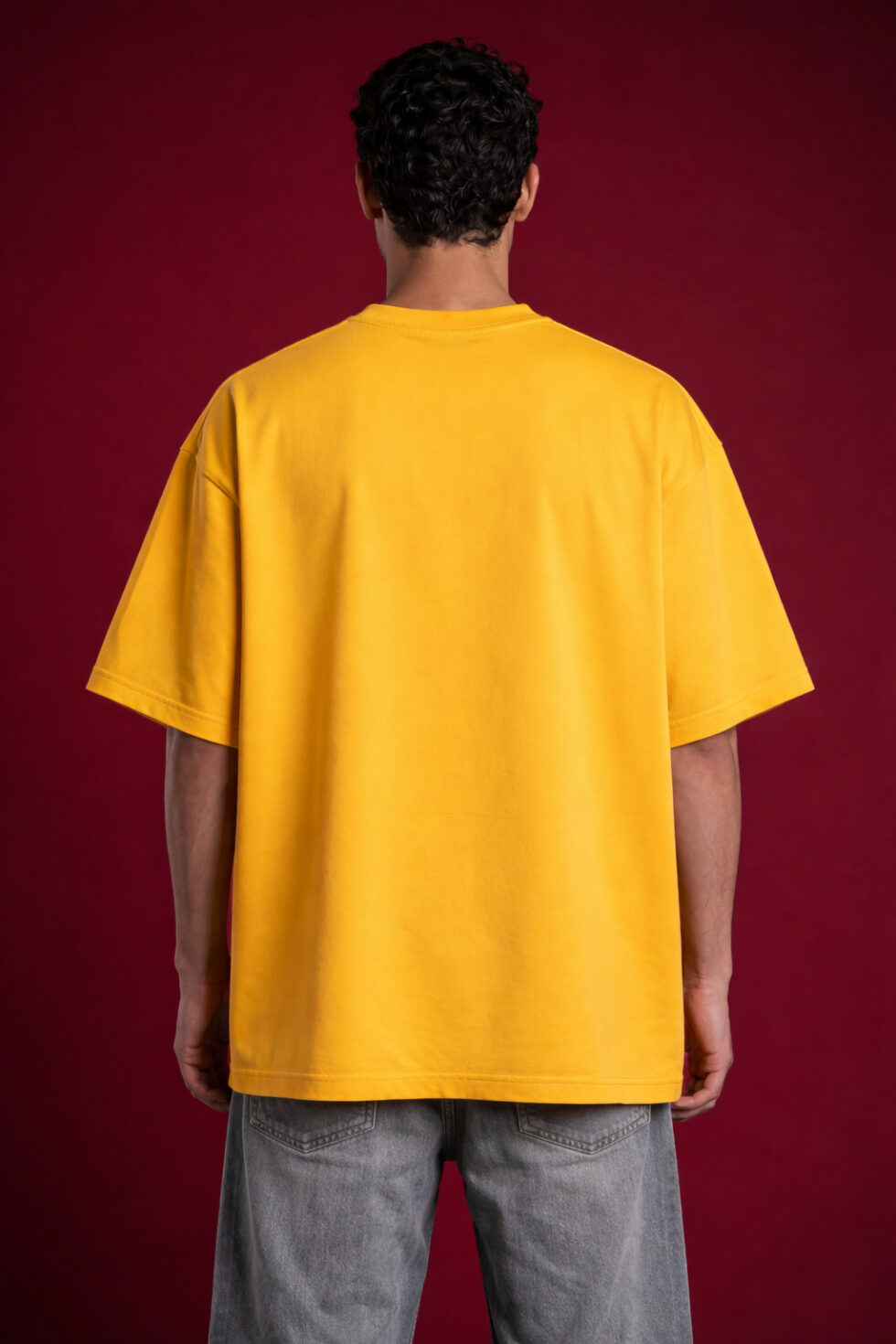 Rear view of a male model wearing a plain oversized yellow streetwear t-shirt with a drop-shoulder design and relaxed boxy fit.