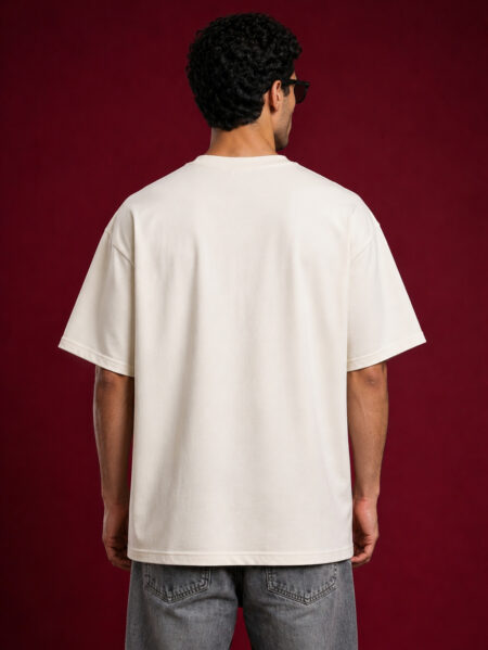 Rear view of a man wearing a cream-colored oversized streetwear t-shirt showing the relaxed dropped-shoulder fit and clean off-white fabric.