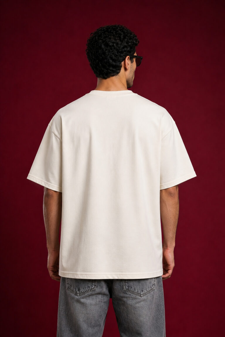 Rear view of a man wearing a cream-colored oversized streetwear t-shirt showing the relaxed dropped-shoulder fit and clean off-white fabric.