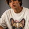 Close-up shot of a male model in a relaxed-fit cream graphic tee showcasing the detailed artwork of a French Bulldog with a red accent