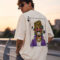 Back view of a man wearing a cream oversized streetwear t-shirt featuring a large cartoon graphic of a character with a gold tooth, leopard bucket hat, and purple jacket inside a playing card frame.