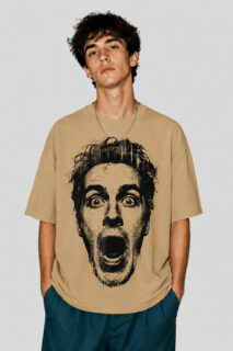 Front view of a male model wearing a beige oversized graphic streetwear t-shirt featuring a large black halftone portrait of a shocked face with an open mouth