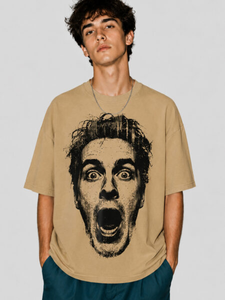 Front view of a male model wearing a beige oversized graphic streetwear t-shirt featuring a large black halftone portrait of a shocked face with an open mouth