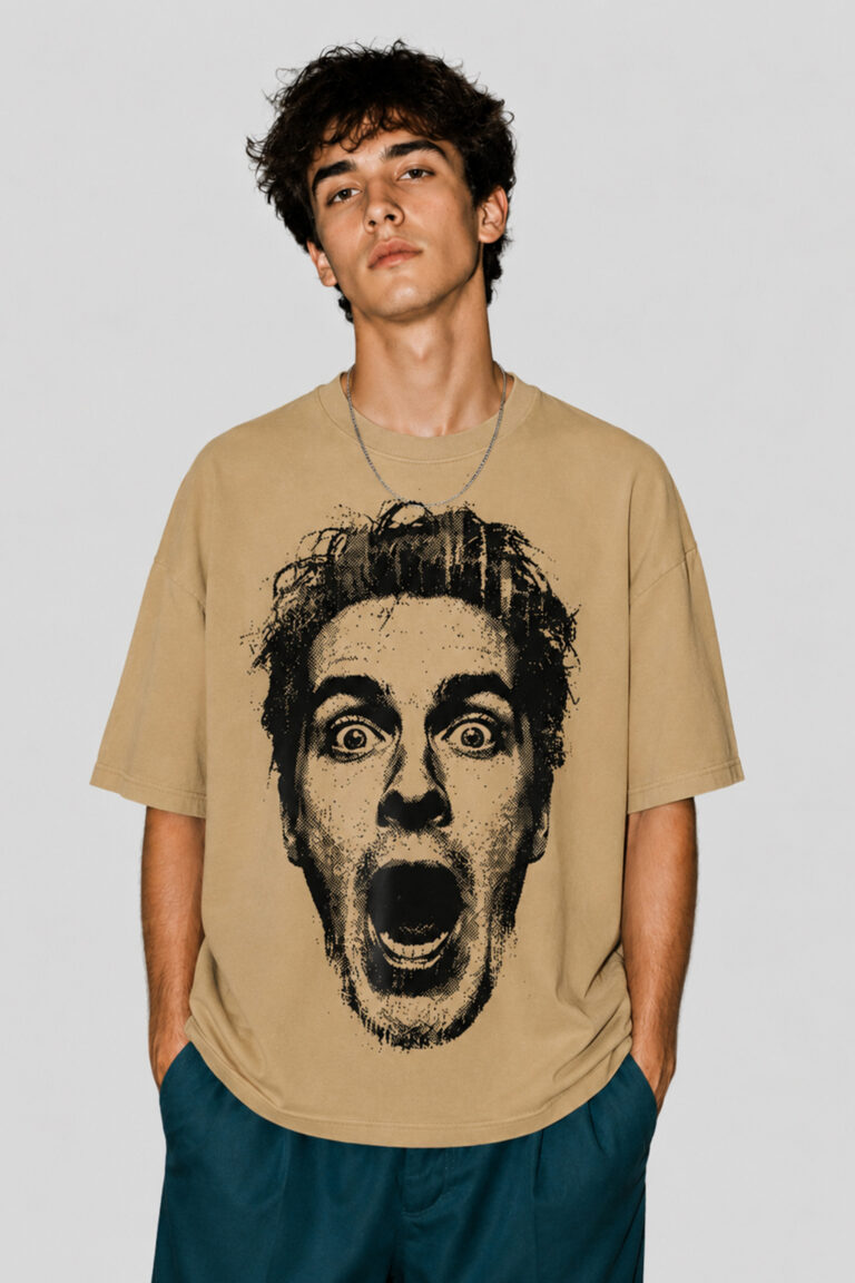 Front view of a male model wearing a beige oversized graphic streetwear t-shirt featuring a large black halftone portrait of a shocked face with an open mouth