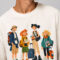 Close-up of the high-definition direct-to-garment print on a cream t-shirt, showing detailed cartoon characters holding luggage with "The Getaway Club" text below.