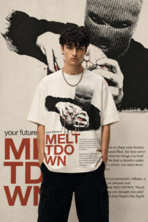 A model wearing an off-white, heavyweight cotton oversized t-shirt featuring a dark, industrial-style graphic of a figure in a balaclava holding a globe, with the text "MELTDOWN" in bold red lettering