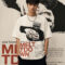 A model wearing an off-white, heavyweight cotton oversized t-shirt featuring a dark, industrial-style graphic of a figure in a balaclava holding a globe, with the text "MELTDOWN" in bold red lettering
